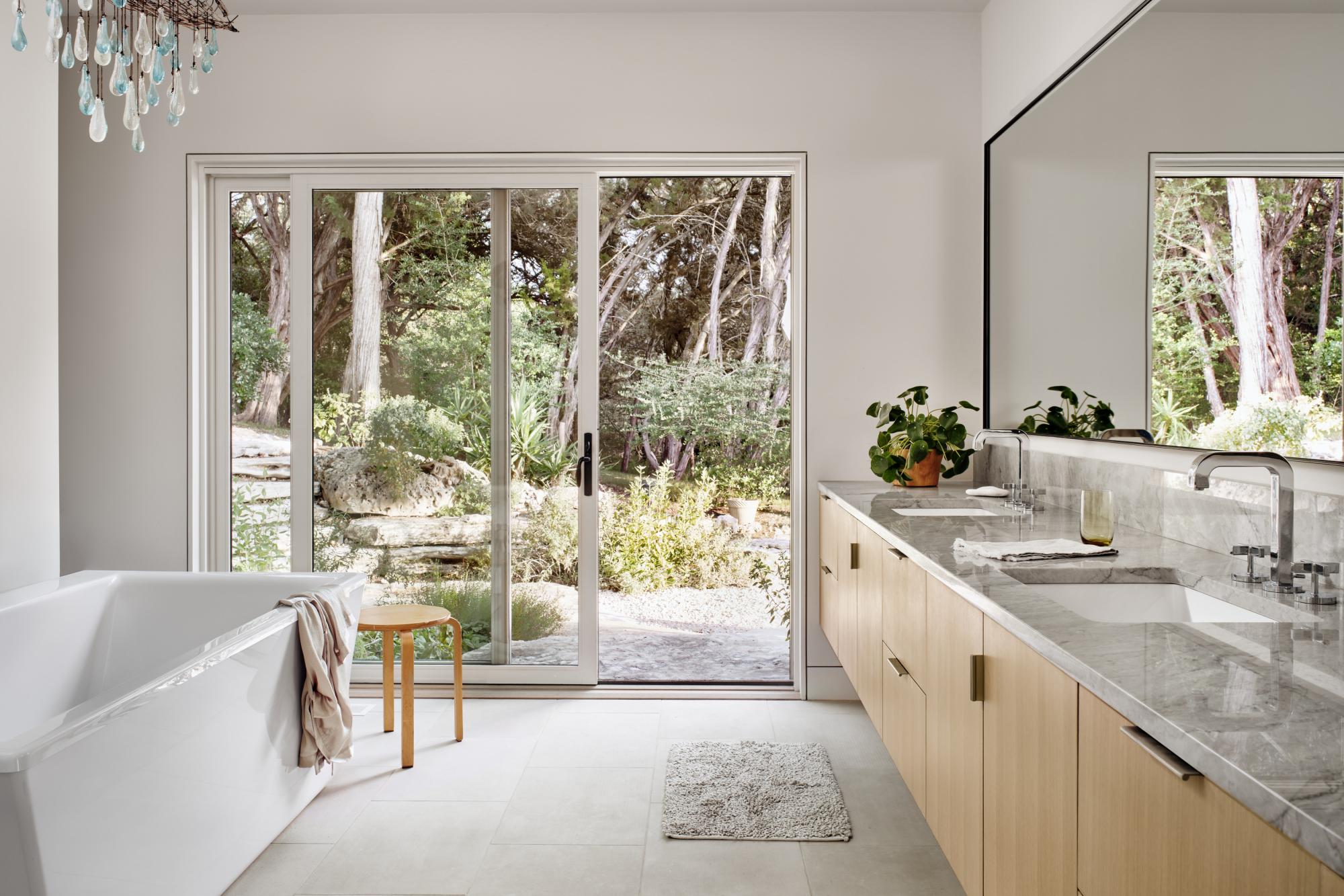 Interior master bathroom connects through a sliding glass door to outdoor landscape 