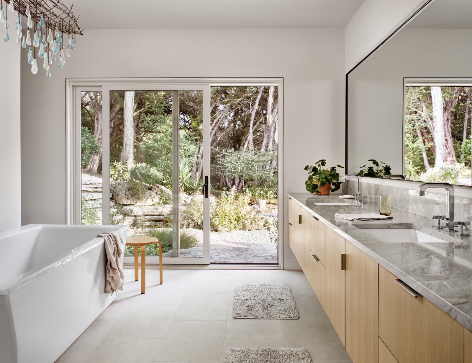 Large master bathroom, features marble, stone, custom chandelier and a sliding glass door connecting to the landscape Interior master bathroom connects through a sliding glass door to outdoor landscape